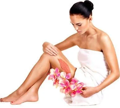 femme brune se caressant la peau de la jambes avec une fleur rose