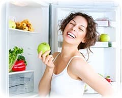 femme blanche avec une pomme verte dans la main devant son frigo
