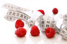 plusieurs framboises autour d'un metre ruban à mesurer sur un fond blanc