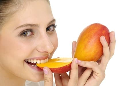 femme mangeant une mangue coupée en deux sur fond blanc
