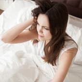 femme brune sur son lit blanc se tenant la tete et les cheveux