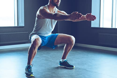 homme an train de faire des squats avec les bras tendus homme an train de faire des squats avec les bras tendus