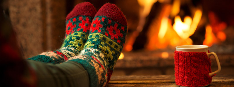 femme avec des chaussettes de Noël à côté du feu avec une tasse de thé